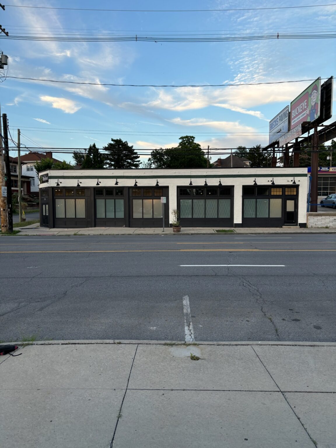 A corner retail building freshly painted white with black trim and brass sconce lighting, finished by BRPainting